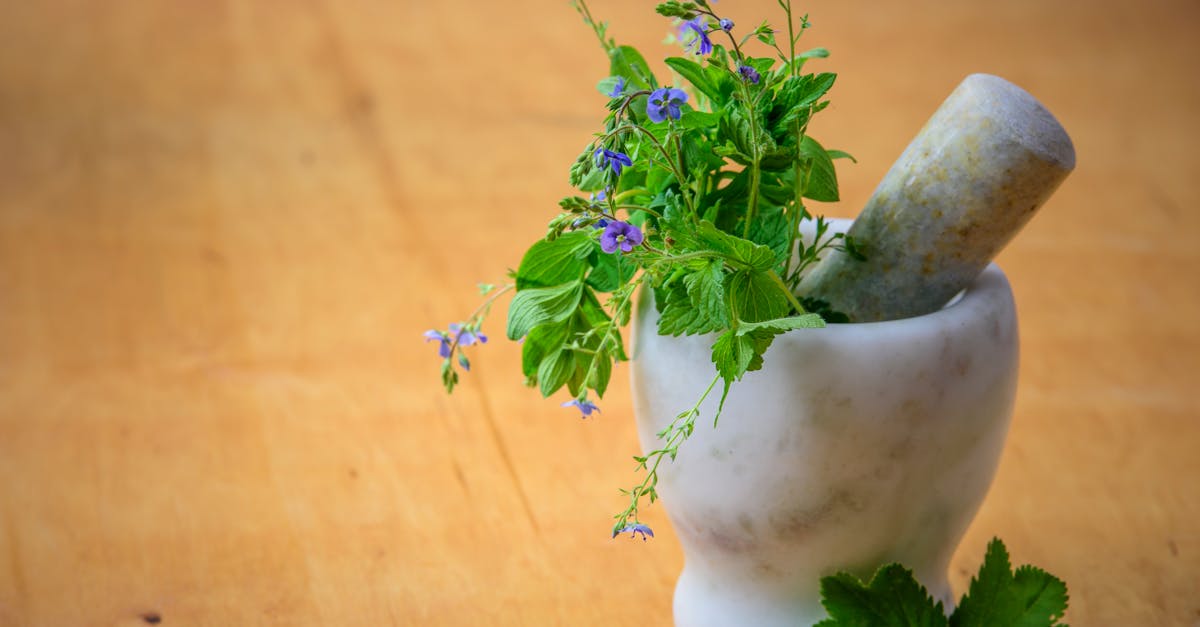 A mortar and pestle filled with various herbs and flowers sitting on a wooden table.
