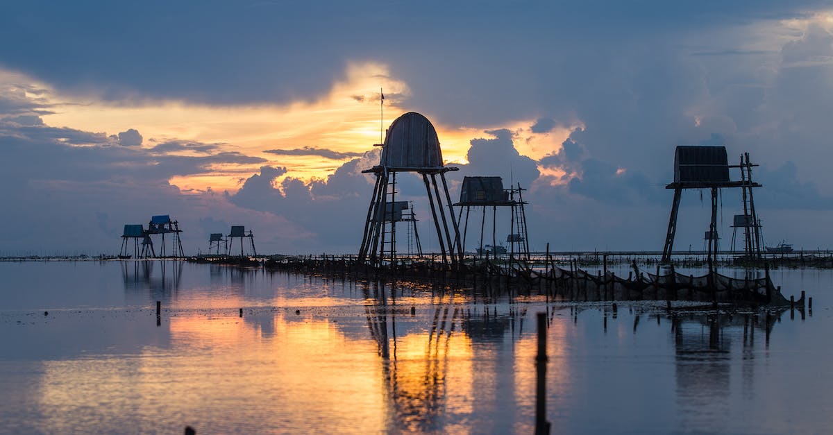 The image shows a row of houses on stilts in the middle of a lake at sunset.