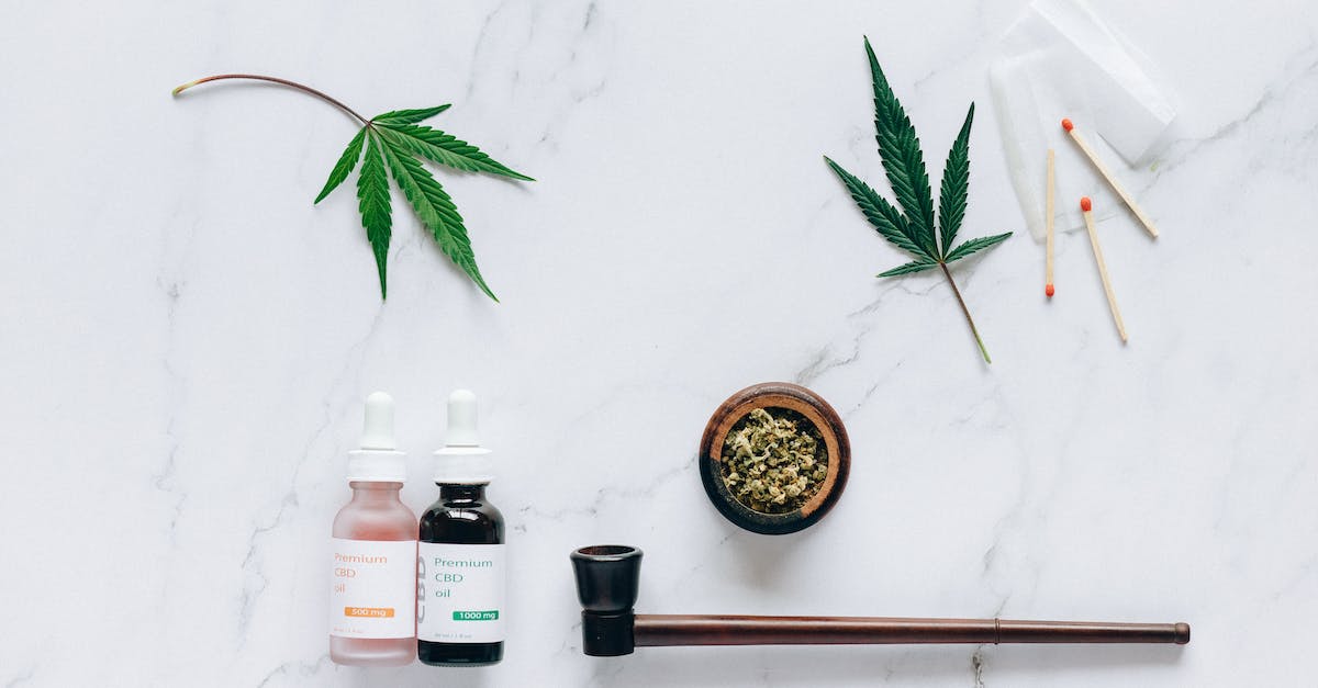 The image shows a table with a bowl of marijuana, a pipe, a bottle of oil, and matches on it.